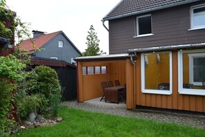 A residential property with a wooden shed, a patio with a table and chairs, and a house with a dark exterior and a tiled roof. - Vrbo Property (Altenau)