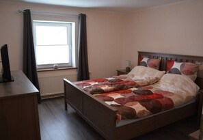 Een slaapkamer met een bed, nachtkastje, raam met gordijnen en een radiator.
