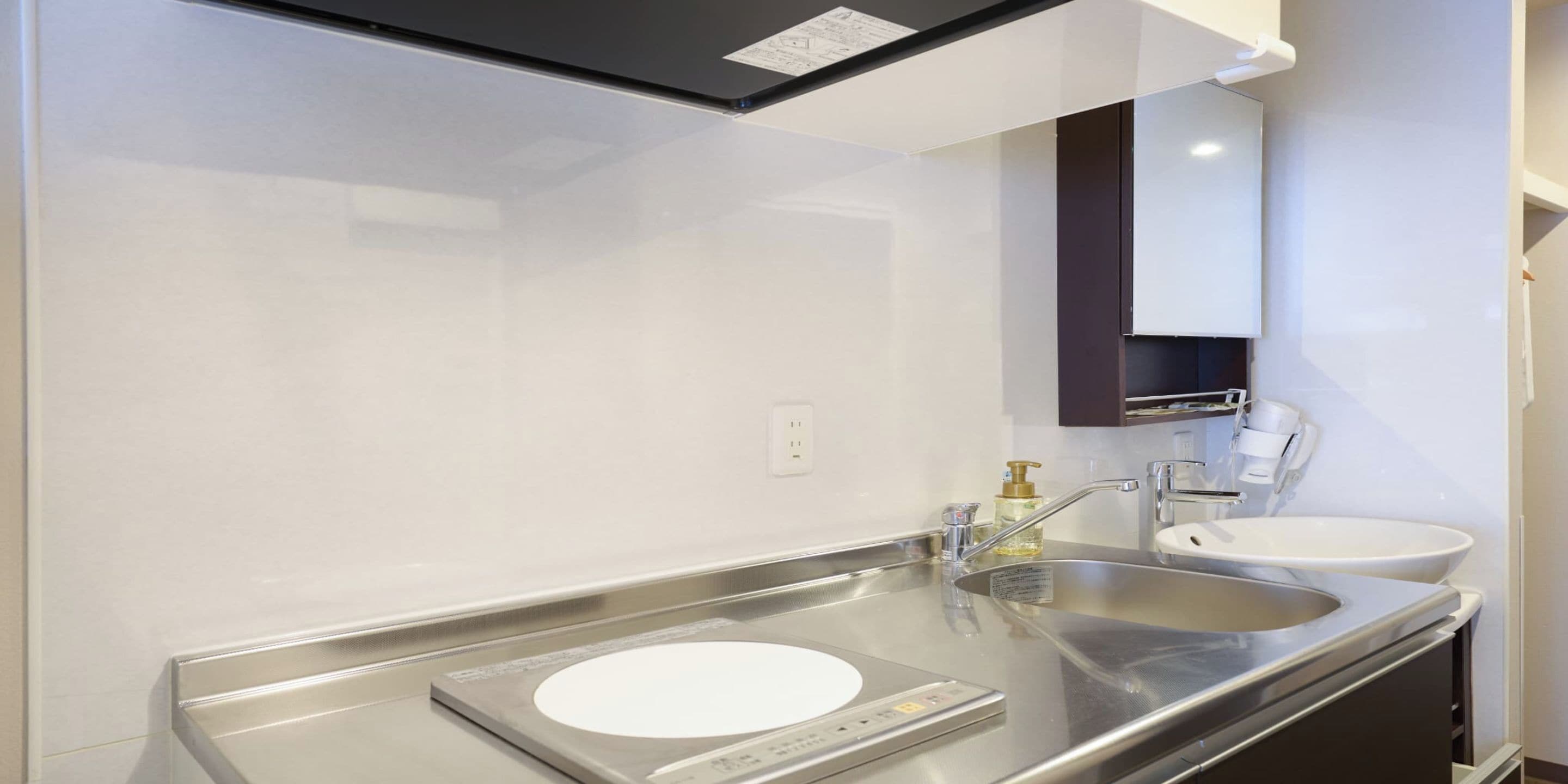A modern bathroom with a stainless steel sink, a mirror, and a soap dispenser.