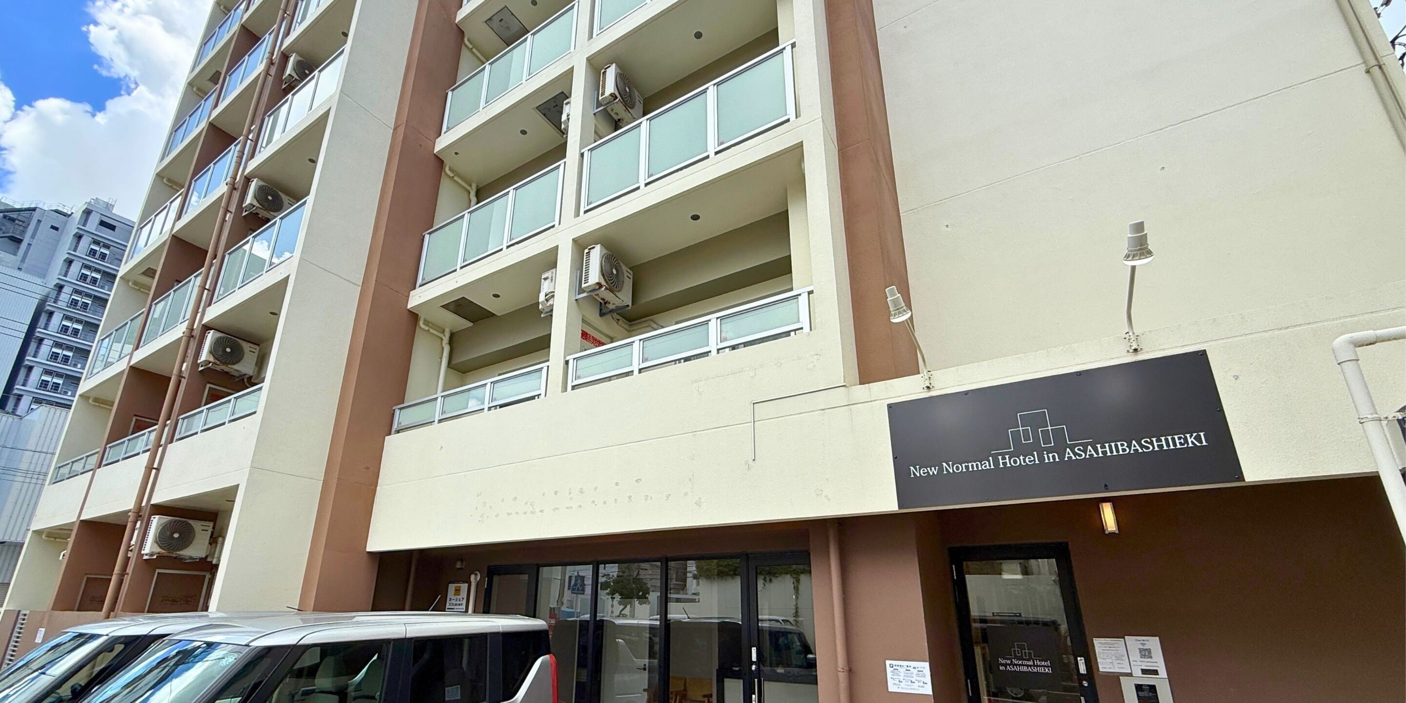 Un edificio de hotel de varios pisos con un cartel que indica que es el New Normal Hotel en Asahibashi.