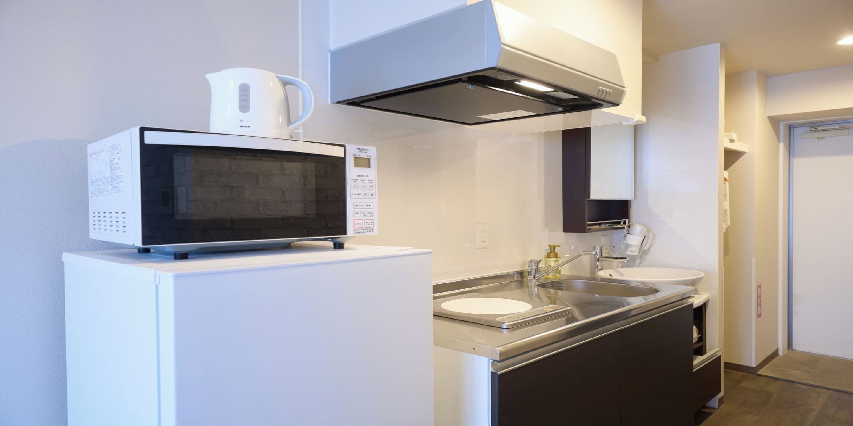 A compact kitchen with a microwave, a coffee maker, and a stainless steel sink.