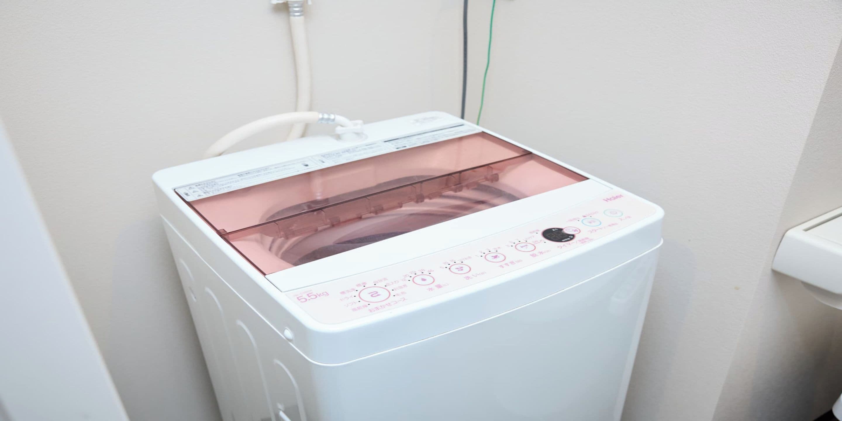 Una lavadora portátil blanca con puerta transparente, panel de control con botones y una pantalla, y un cable de alimentación.