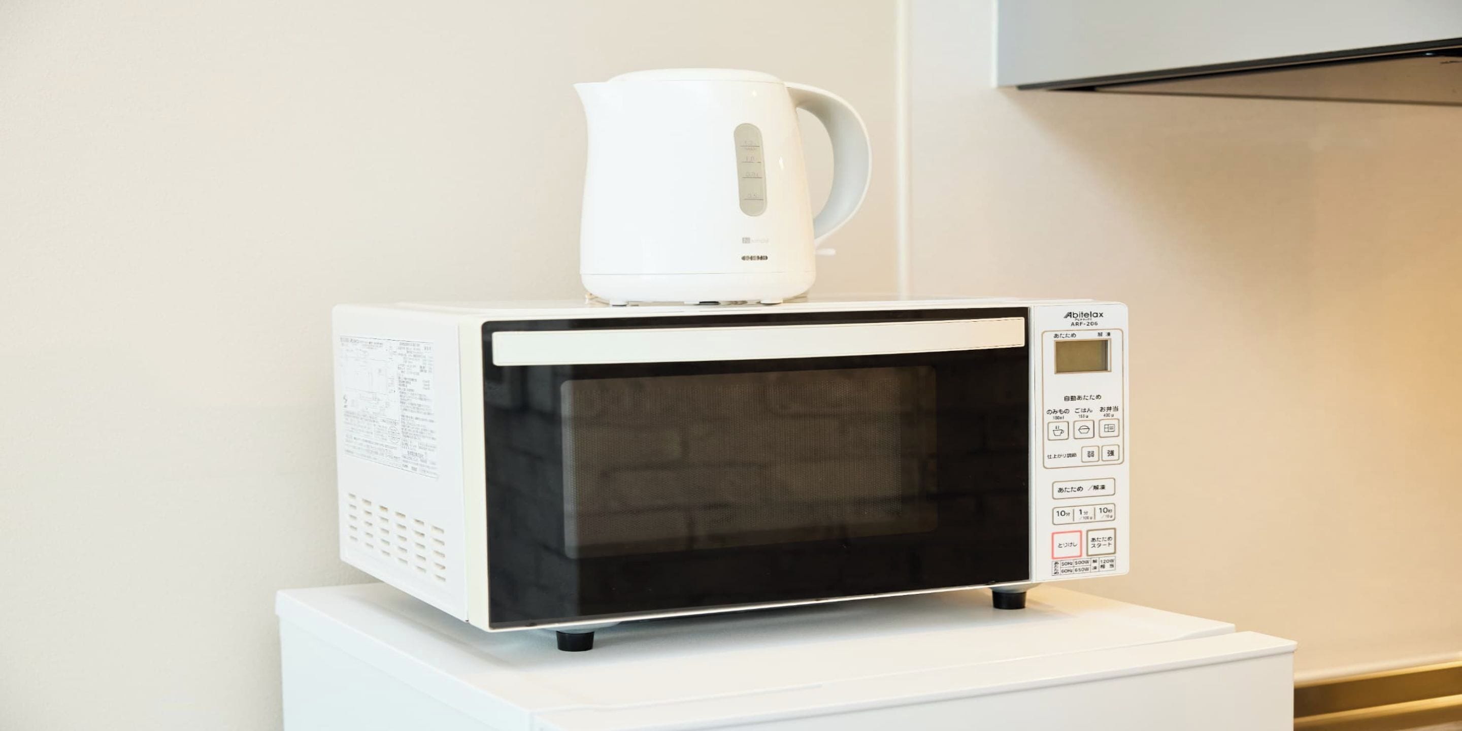 A microwave oven with a kettle on top, placed on a white stand.