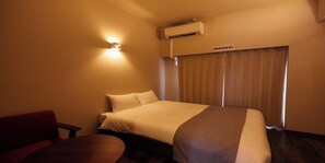 Habitación de hotel con cama, escritorio y silla. Se observa un equipo de aire acondicionado en la pared y un cartel sobre la cama.