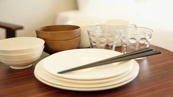 Una mesa de comedor con platos blancos apilados, un cuenco de madera y dos vasos de vidrio.