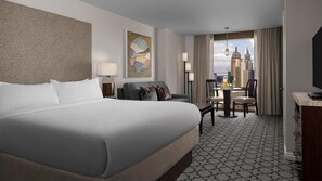 A hotel room with a large bed, a desk, a chair, a TV, a painting on the wall, and a view of a cityscape. - MARRIOTT GRAND CHATEAU (Las Vegas)