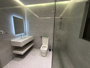A modern bathroom with a glass-enclosed shower, a white toilet, and a vanity with a mirror. - 103 JRE comfortable and accessible retreat (Amman)