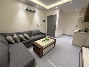 Een moderne woonkamer met een grijze bank, een houten salontafel en een keukenhoek met een spoelbak en kasten.