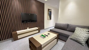 Un soggiorno moderno con televisione a schermo piatto, un divano grigio, un tavolino da caffè e un cuscino decorato.