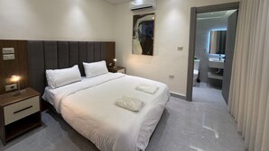 Ein modernes Hotelzimmer mit einem großen Bett, Nachttischen, einer Klimaanlage, einem Gemälde und einem durch eine offene Tür einsehbaren Badezimmer.
