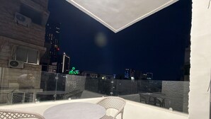 Eine Dachterrasse mit einem runden Tisch und zwei Korbstühlen mit Blick auf eine nächtliche Skyline.