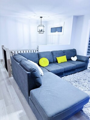 En moderne stue med en modulsofa, en lille skammel, en hvid radiator, en grå måtte og en hængende lampe.