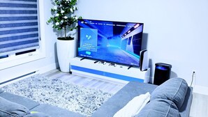 Una habitación moderna con un televisor de pantalla plana grande, un sofá, una planta en maceta y una ventana con persianas.