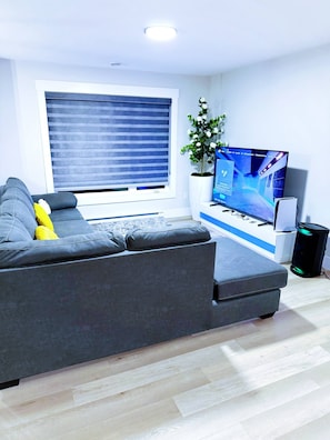 En moderne stue med en grå sofa, et fladskærms-tv, en Sony-højttaler og en potteplante.
