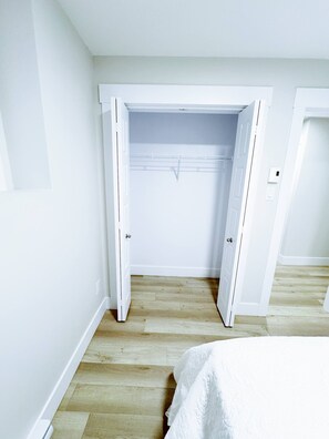 Ein Schlafzimmer mit Holzboden, weißen Wänden und einem offenen Kleiderschrank.