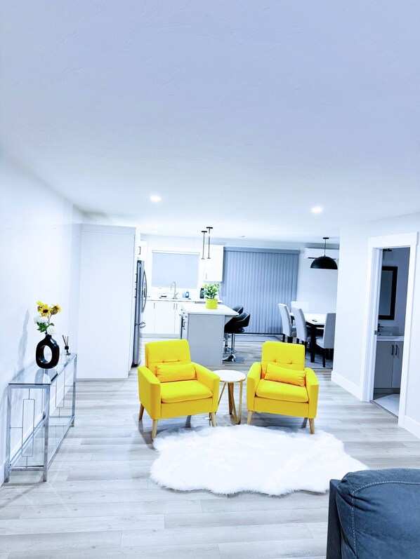 A modern living room with two yellow armchairs, a white fur rug, and a glass console table with a vase of flowers. - Luxury 3-Bedroom Full House Near Magnetic Hill (Moncton)