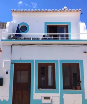 Un edificio de dos pisos con un balcón, un ventanal circular en el piso superior y una puerta en la planta baja.