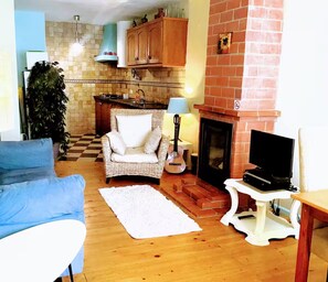 Una sala de estar con un sofá azul, una silla de mimbre, un tapete blanco, una chimenea y un televisor sobre un mueble.