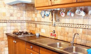 Una cocina con estufa a gas, dos fregaderos, armarios de madera y salpicadero de azulejos.