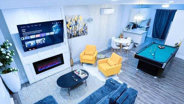 A modern living room with a blue sofa, yellow armchairs, a pool table, and a flat-screen TV mounted on the wall. - Modern 3-Bedroom Retreat Near Moncton Hospital and Downtown (Moncton)
