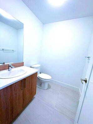 A bathroom with a sink, mirror, toilet, and shower area. - Stylish 3-Bedroom Full House Near Magnetic Hill (Moncton)
