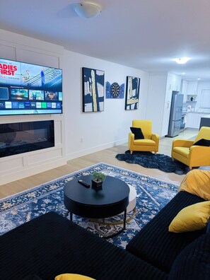 A modern living room with a flat-screen TV, yellow armchairs, a black coffee table, and abstract wall art. - Stylish 3-Bedroom Full House Near Magnetic Hill (Moncton)