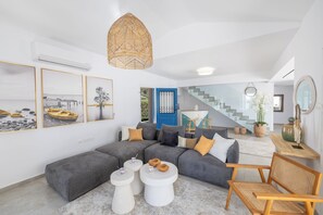 Ein modernes Wohnzimmer mit einem grauen Ecksofa, weißen Couchtischen und einer Pendelleuchte aus Weidengeflecht.