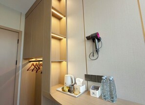 Habitación de hotel con armario de madera, mesita de noche con cafetera, caja de pañuelos y agua embotellada.