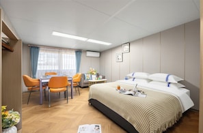 Hotellihuone, jossa on sänky, työpöytä, tuoleja ja ikkuna, jossa on verhot.
