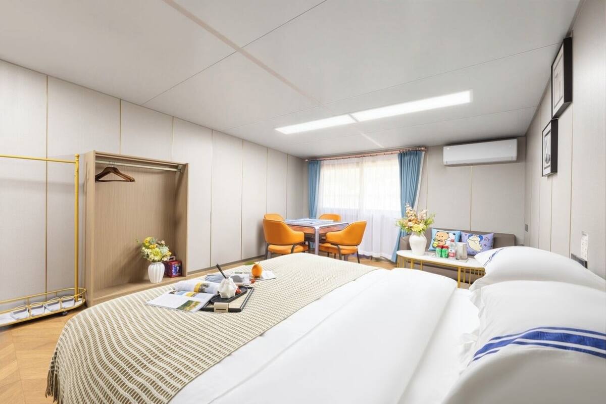 Hotellihuone, jossa on sänky, työpöytä, kaksi tuolia, vaatekaappi ja ikkuna, jossa on verhot.