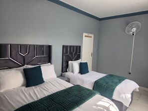 Twee bedden met hoofdborden, een ventilator en een deur.