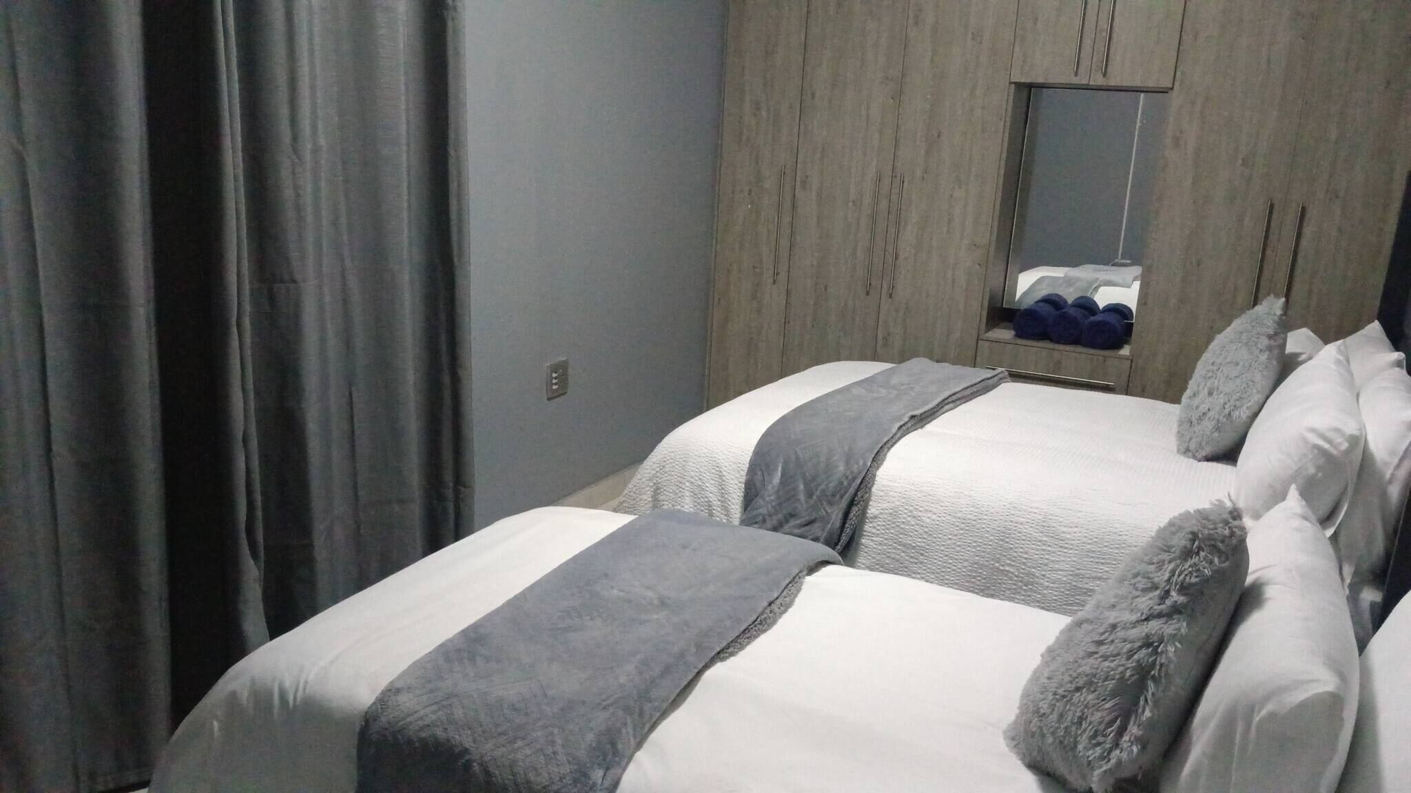 Une chambre d’hôtel avec deux lits, une literie grise et blanche, un mur en bois, un miroir et une fenêtre.