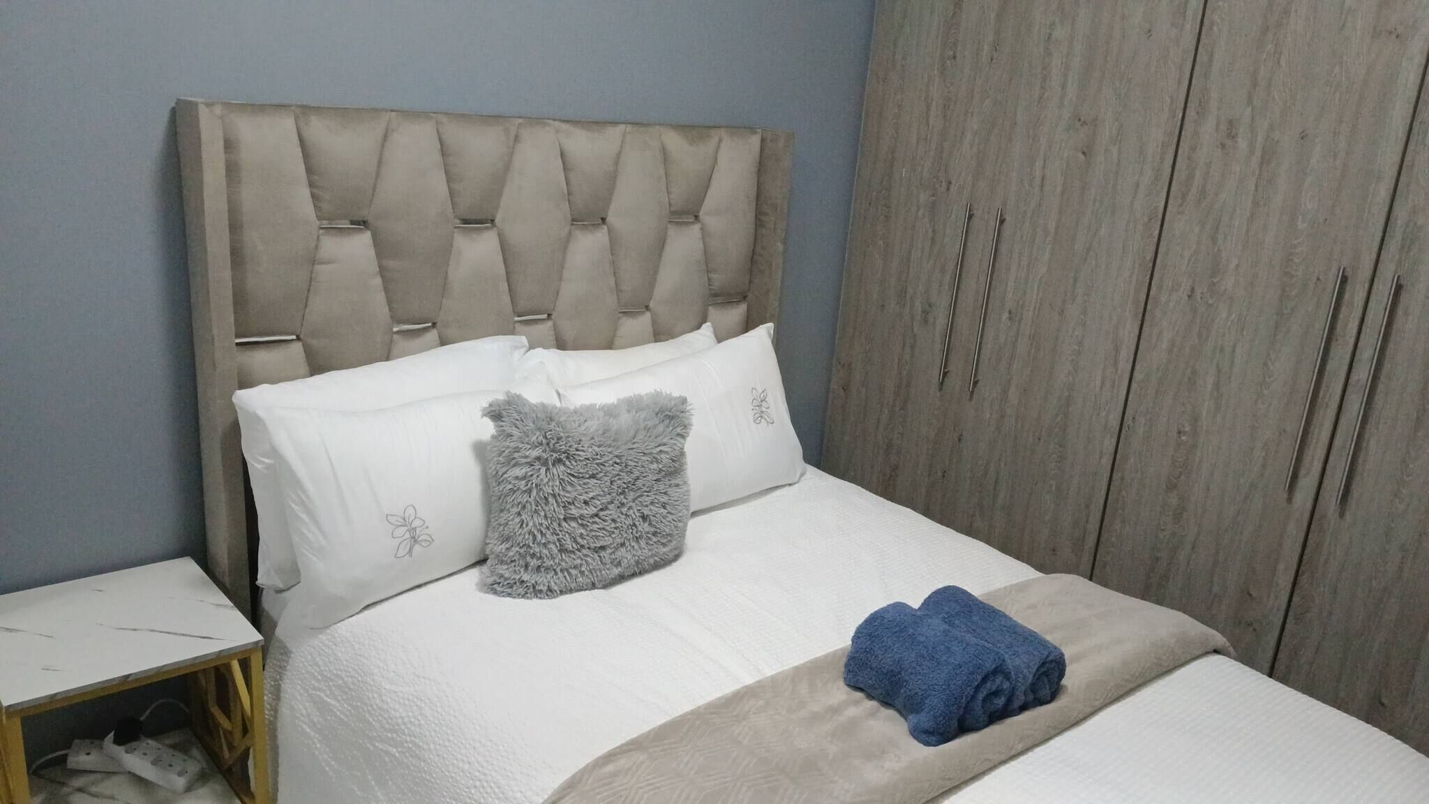 Een bed met een gestoffeerd hoofdbord, wit beddengoed, een grijs zacht kussen en een blauwe handdoek.