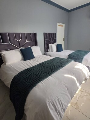 Een hotelkamer met twee bedden, een deur en een betegelde vloer.