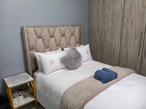 Een bed met een gestoffeerd hoofdbord, witte beddengoed en een blauwe handdoek.