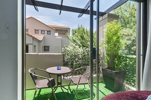 A balcony with a table and chairs, a potted plant, and a view of a building with a tiled roof. - Zalari Loft B, Nature-Inspired 2 Bed Loft Paulshof (Sandton)