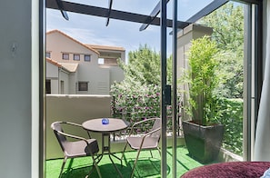 A balcony with a table and chairs, a potted plant, and a view of a building with a tiled roof. - Zalari Luxe Loft B, Nature 1-Bed Loft, Paulshof (Sandton)