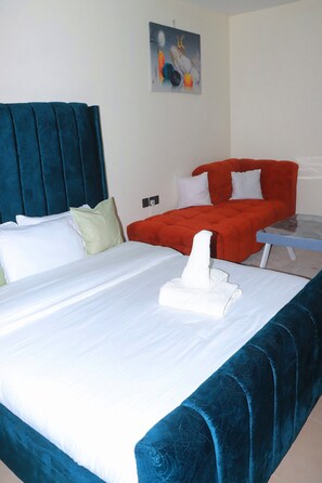 Habitación de hotel con cama, sofá rojo, una mesita y un cuadro en la pared.