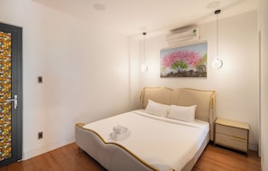 Quarto com cama, mesa de cabeceira, ar condicionado fixado na parede e um quadro de uma árvore.