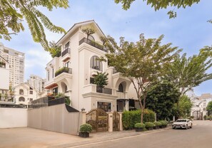 A multi-story residential building with balconies, a gated entrance, and a parked car. - Garden Oasis Pool Villa with 10 Bedrooms (Ho Chi Minh City)