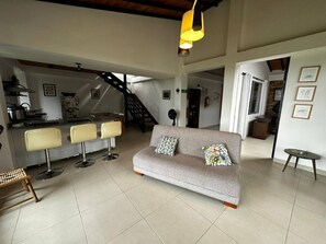 A spacious living area with a sofa, two bar stools, a dining table, and a staircase. - Country House in Quindío – Casa Victoria (Calarcá)