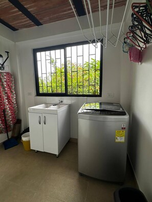 A compact kitchen with a window, a washing machine, and a sink. - Country House in Quindío – Casa Victoria (Calarcá)