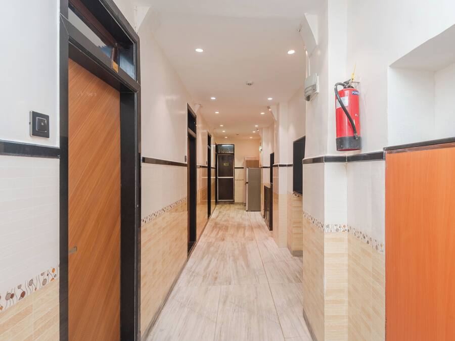 Un pasillo de hotel con un extintor de incendios fijado en la pared, una puerta a la izquierda y un pasillo que conduce a una habitación.
