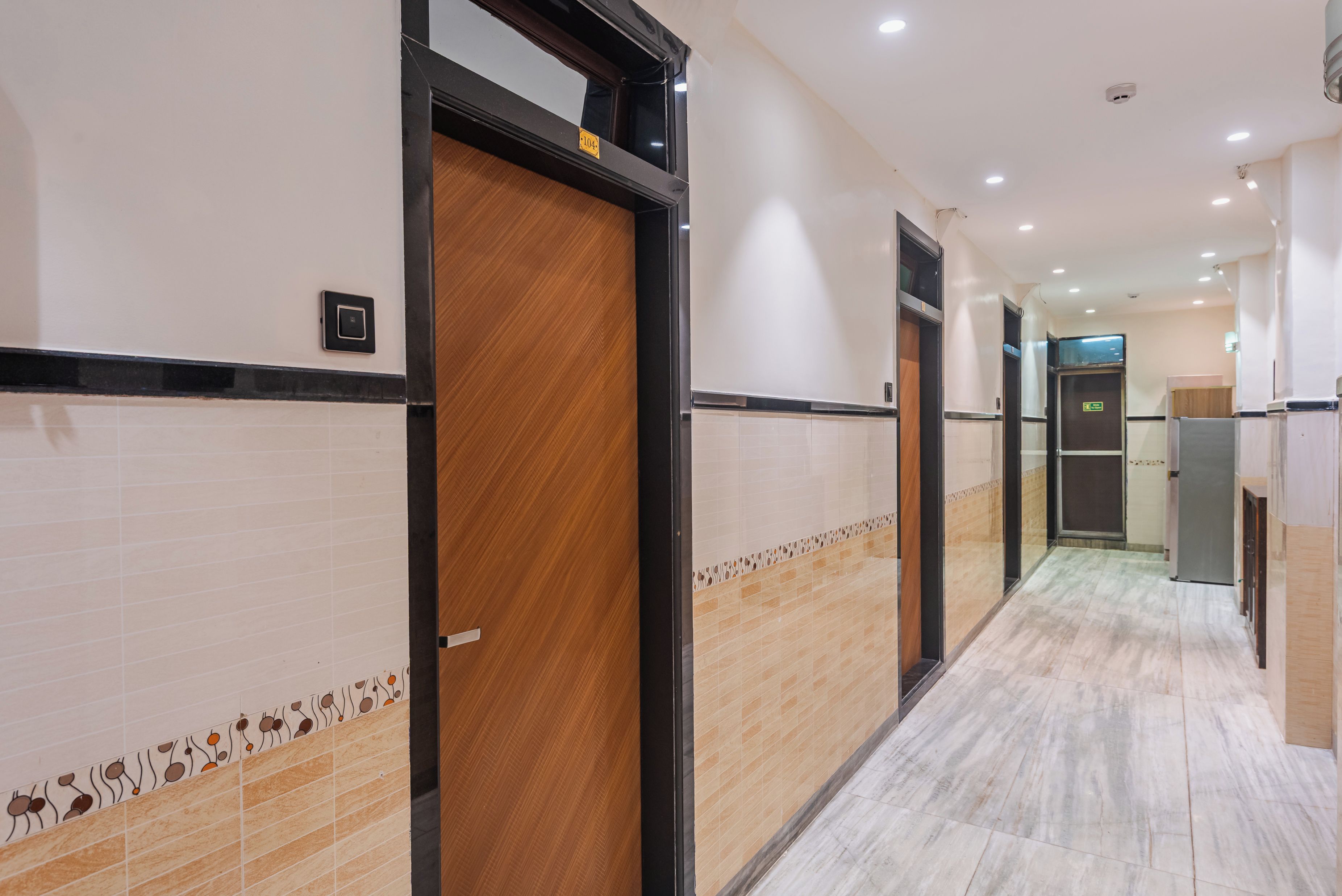 A hotel corridor with wooden doors, tiled walls, and a marble floor.