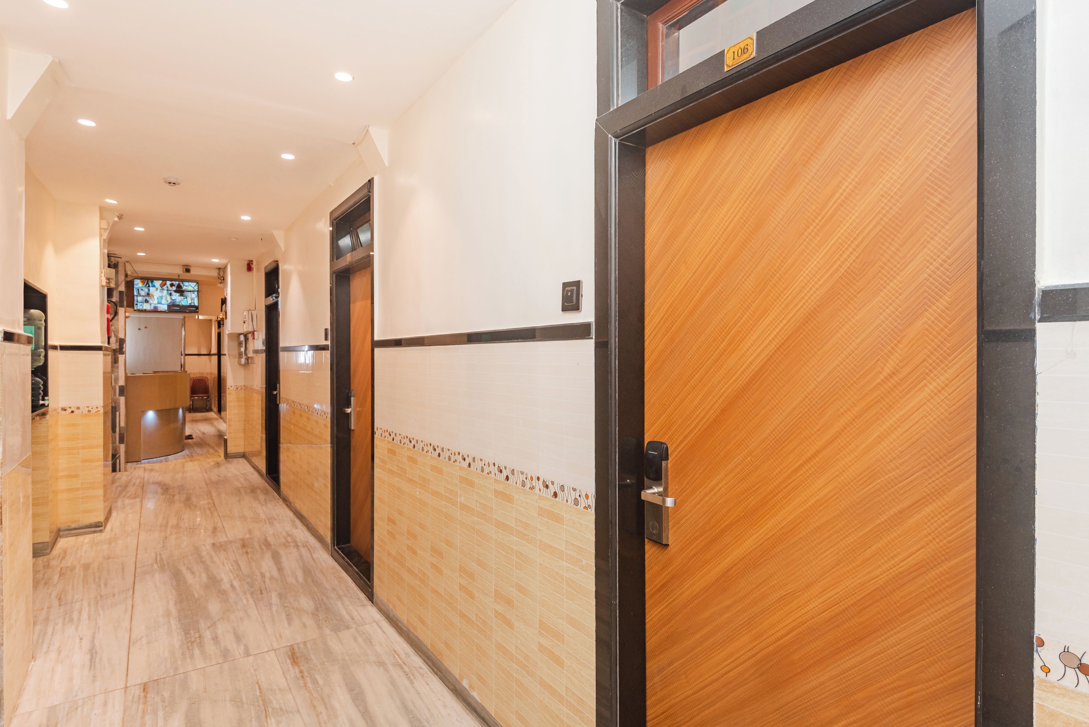 A hotel corridor with wooden doors, tiled walls, and a tiled floor.
