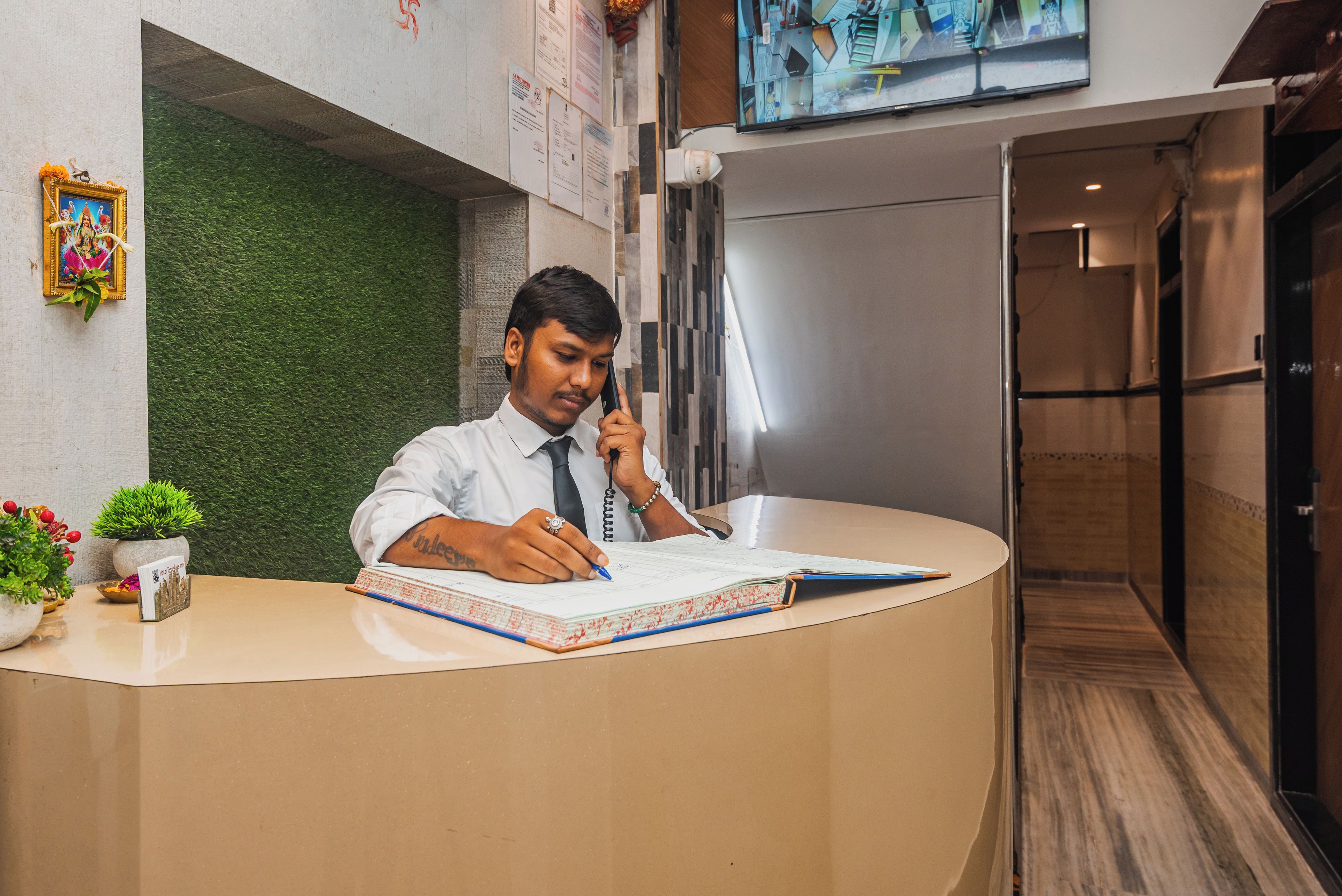 A reception desk with a person writing, a green wall, a TV screen, and a wooden floor.