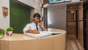A reception desk with a person writing, a green wall, a TV screen, and a wooden floor.