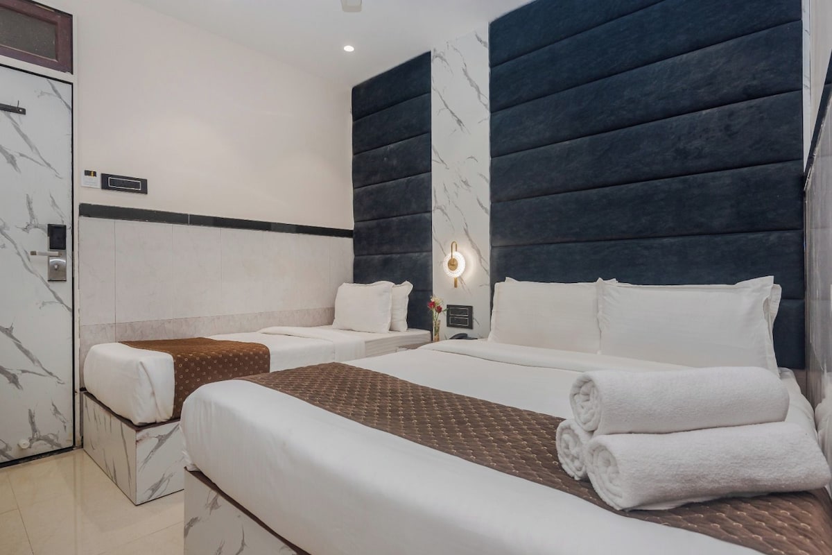 A hotel room with two beds, a minibar, a marble-patterned wall, and a modern light fixture.