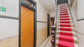 Un pasillo de hotel con una puerta de madera, una escalera con alfombra roja y una pared de azulejos.