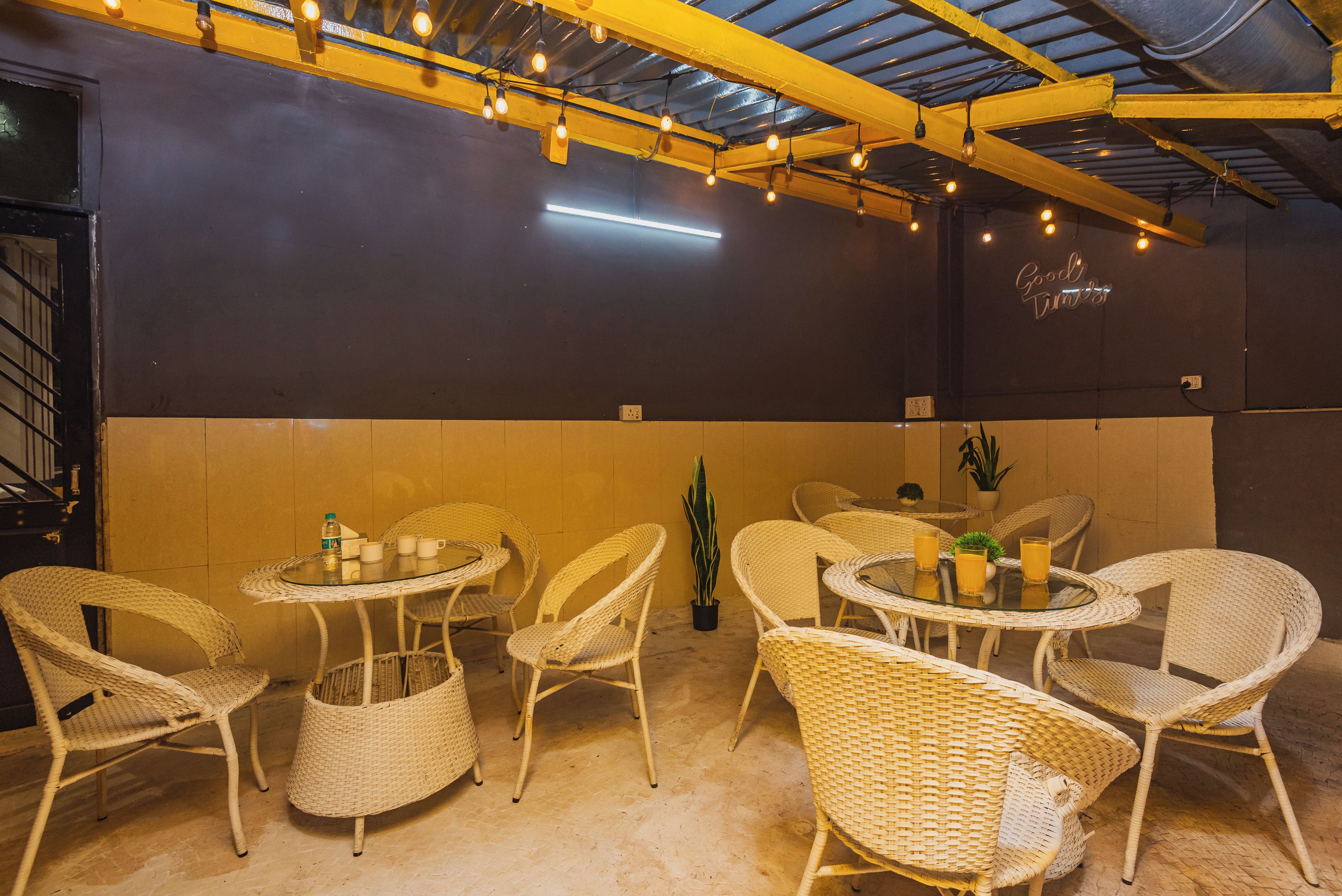 A dining area with round tables and wicker chairs, a potted plant, and a neon sign on the wall.